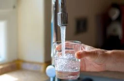 59848142 - woman filling a glass of water from a stainless steel or chrome tap or faucet, close up on her hand and the glass with running water and air bubbles