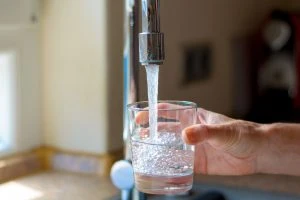 59848142 - woman filling a glass of water from a stainless steel or chrome tap or faucet, close up on her hand and the glass with running water and air bubbles